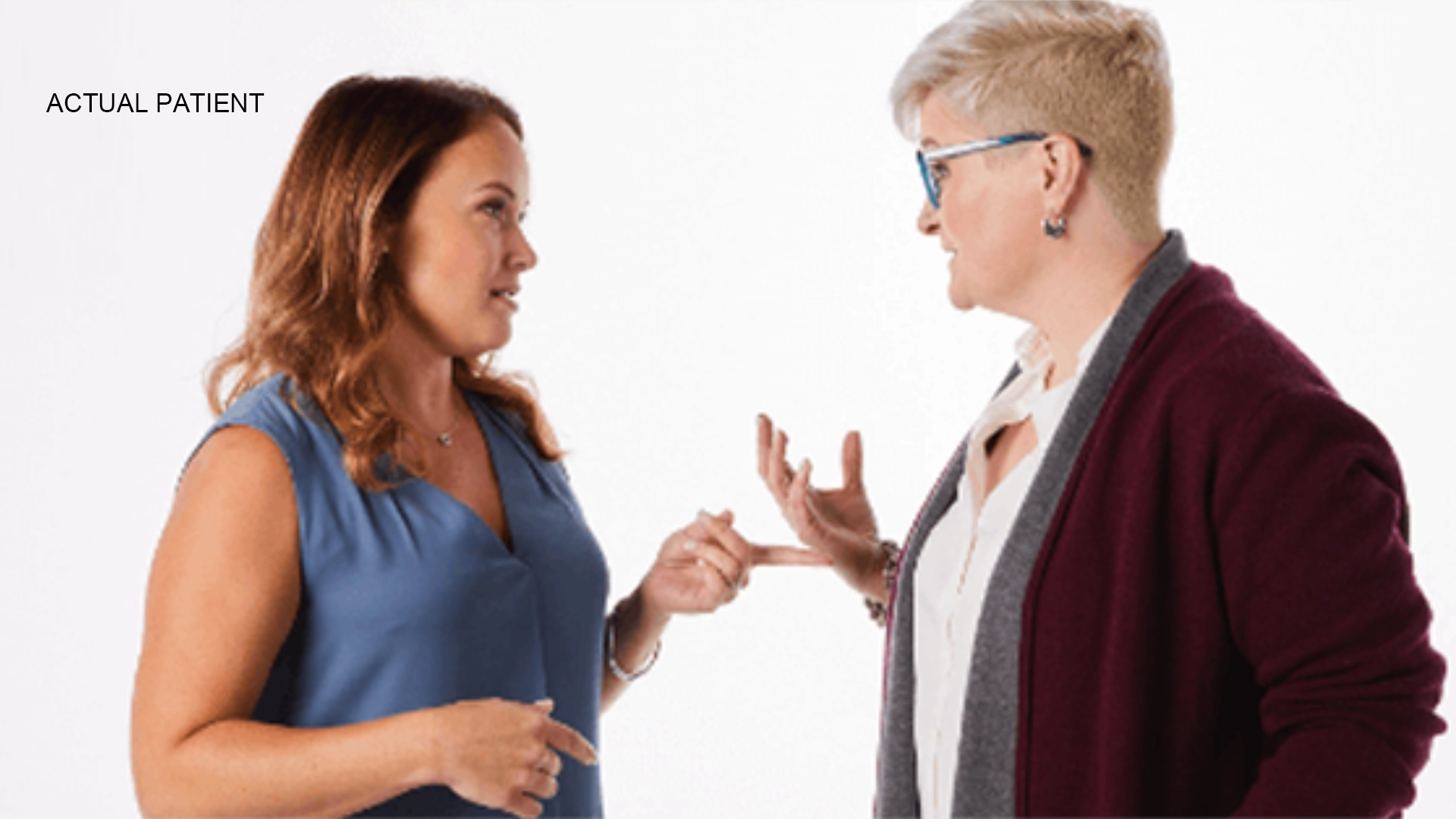 Two individuals talking to each other in front of a white background.