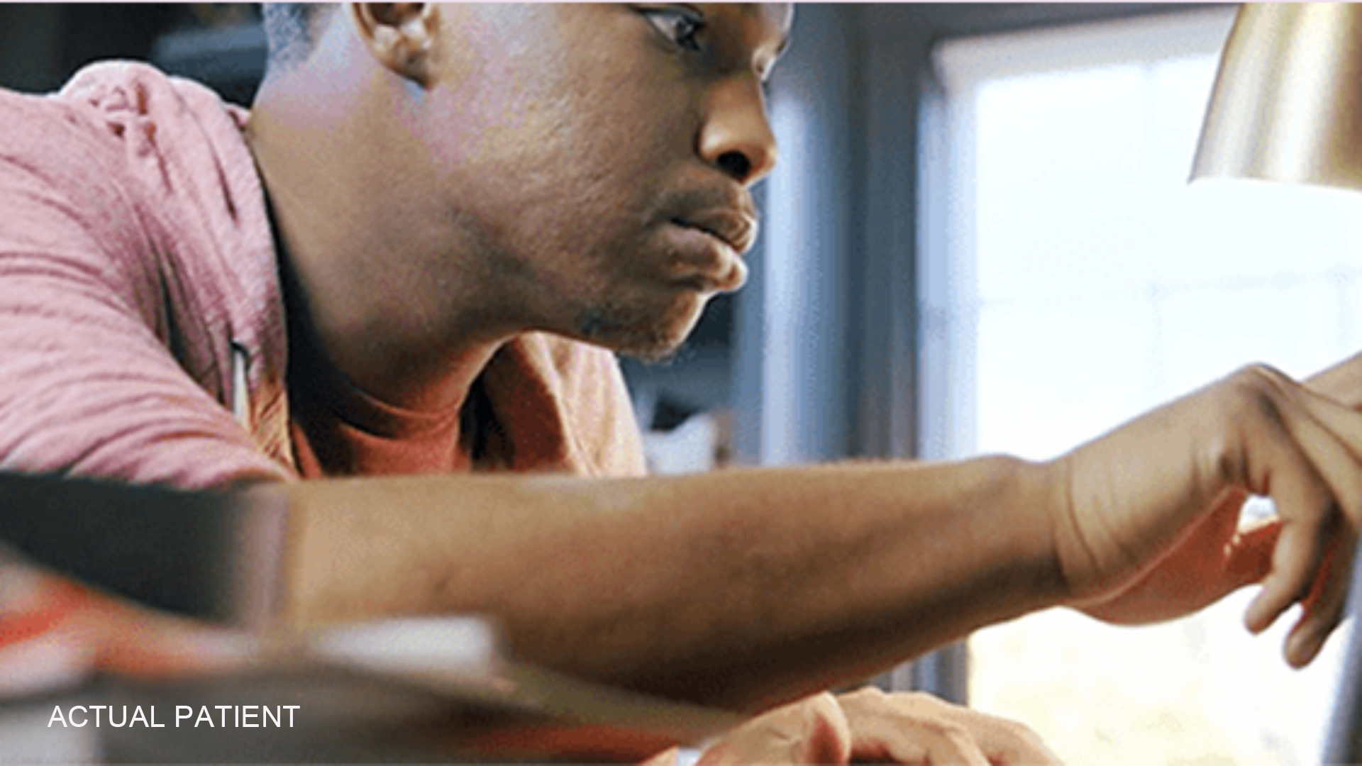 A man wearing a pink hoodie is working on a desktop in front of a blurred background.