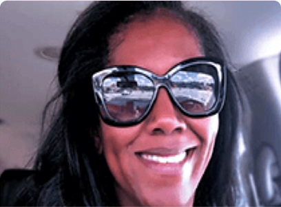 A smiling woman wearing oversized sunglasses inside a car.