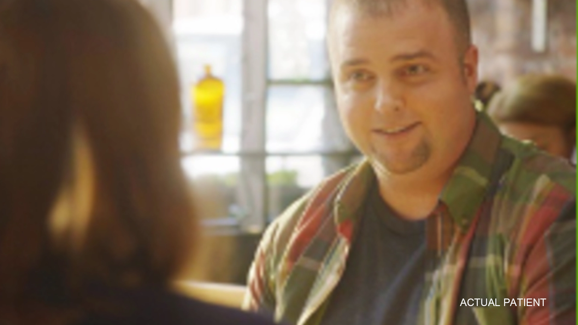 A short-bearded man talking to someone, with a yellow bottle in the background.