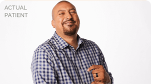 A smiling man wearing a checked shirt standing in front of a white background.