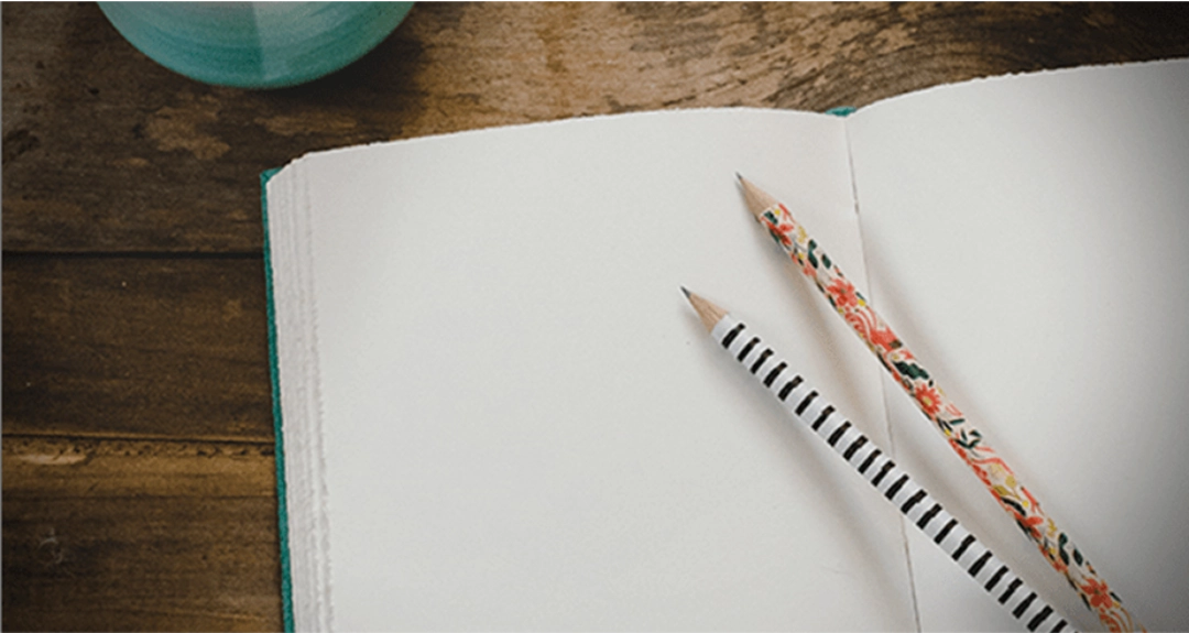 A plain white open notebook with two pencils placed on top.