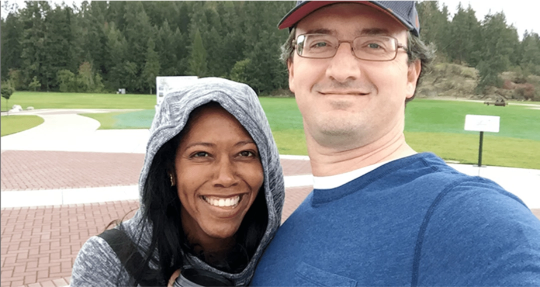 A couple standing together with greenery in the background.