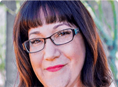 A woman is wearing glasses, with greenery in the background.