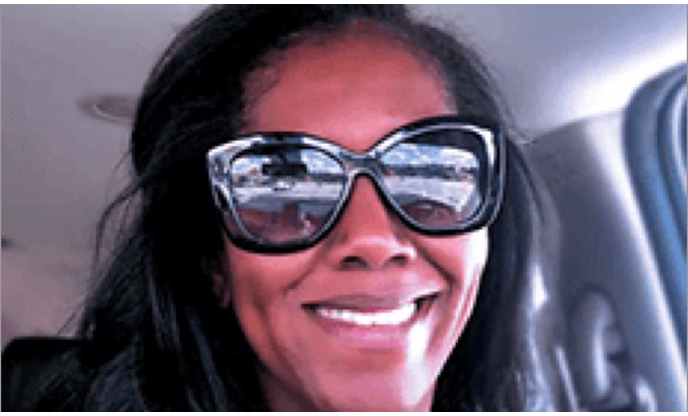 A smiling woman wearing oversized sunglasses inside a car.