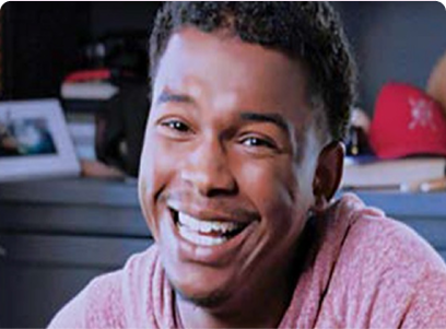 A smiling man with sports equipment and books in the background.
