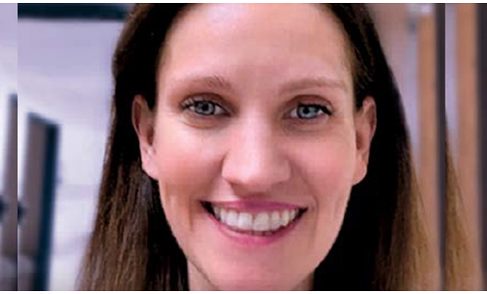 A woman with brown hair is smiling with a blurred background.
