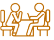 Icon of two people sitting at a table, one using a laptop in orange.