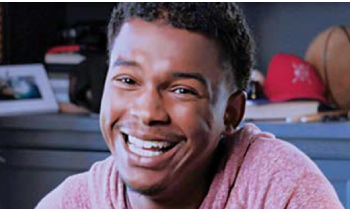 A smiling man with sports equipment and books in the background.